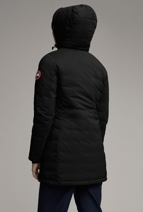 A person is seen from the rear wearing a long, black hooded jacket with a circular red, white, and blue logo on the left sleeve.