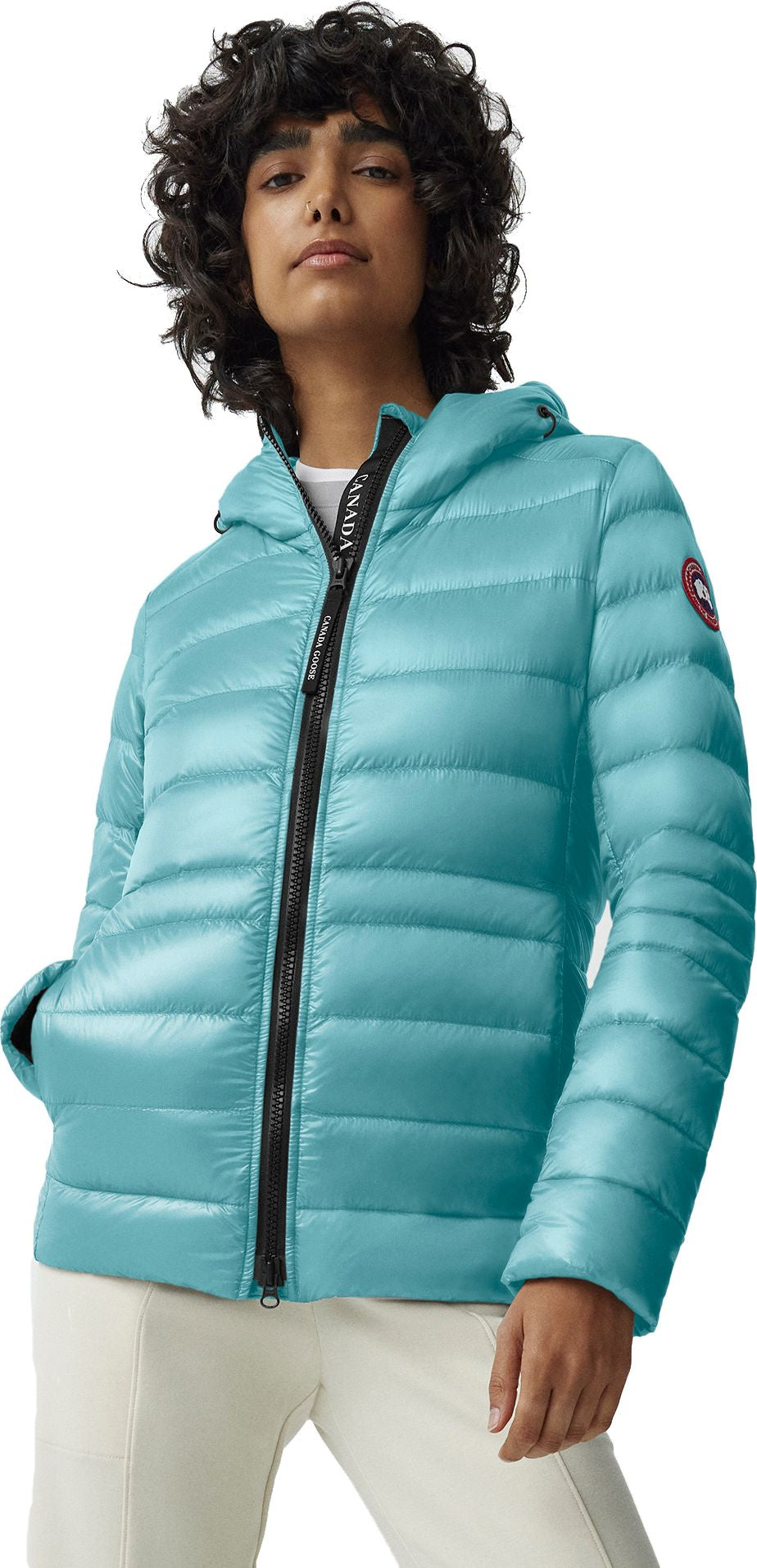 A woman wearing a turquoise, hooded puffer jacket with a black zipper.