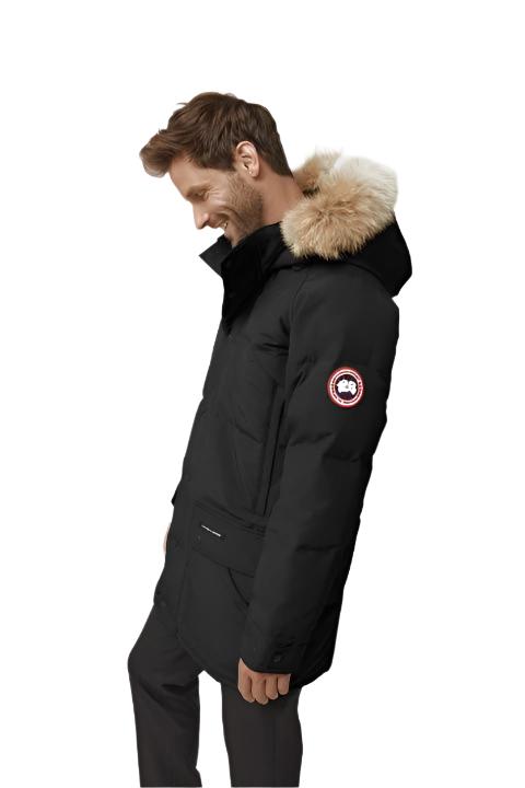 Man wearing a black parka with a fur-trimmed hood and a circular logo patch on the left arm.