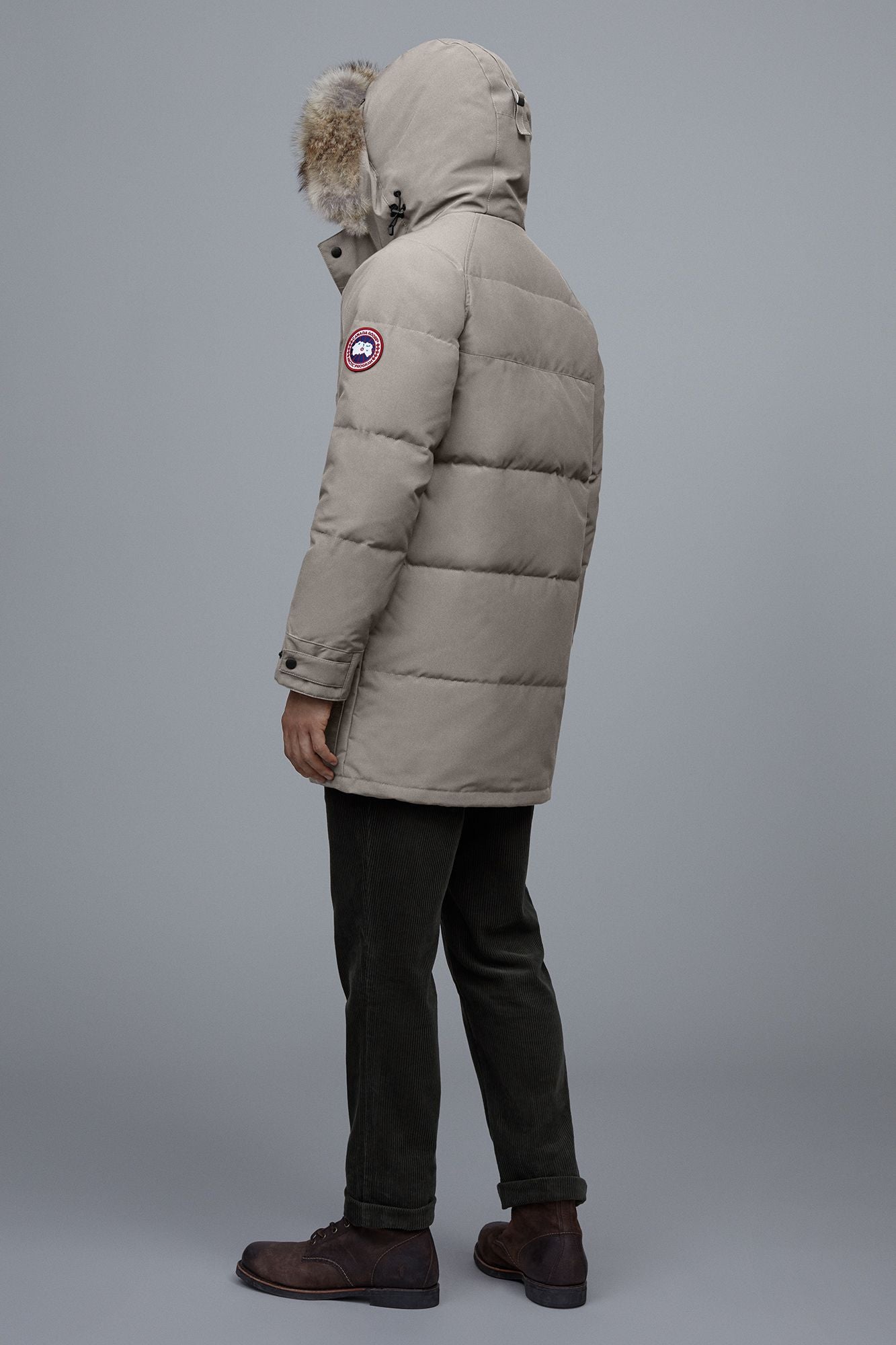 Person wearing a tan, mid-thigh length puffer coat with a hood trimmed with fur.