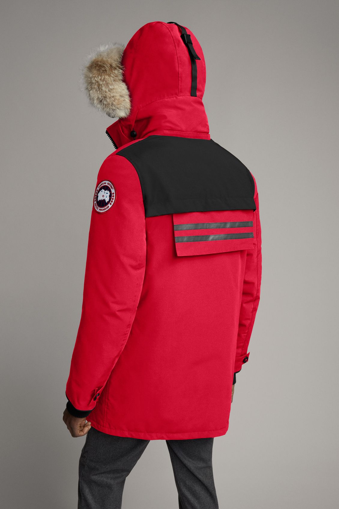A red winter parka with a fur-lined hood, black shoulder and back yoke, and the circular logo patch on the left sleeve.