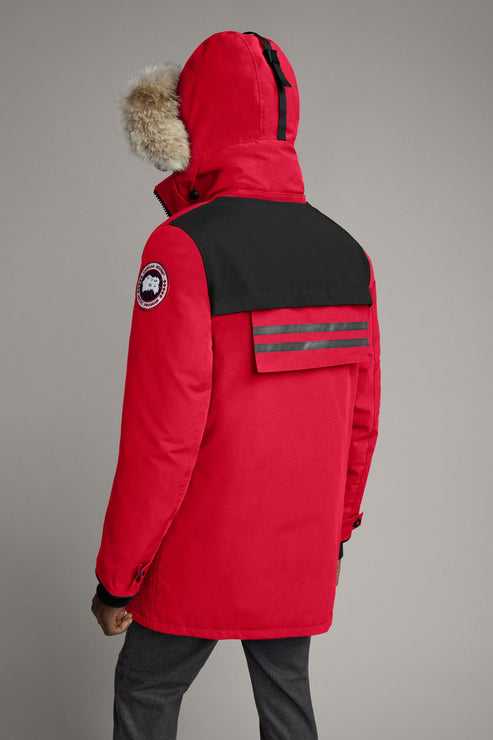 A red winter parka with a fur-lined hood, black shoulder and back yoke, and the circular logo patch on the left sleeve.