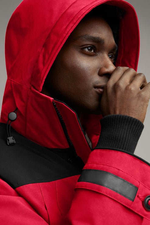 Man in red hooded jacket with black accents, hand near face.