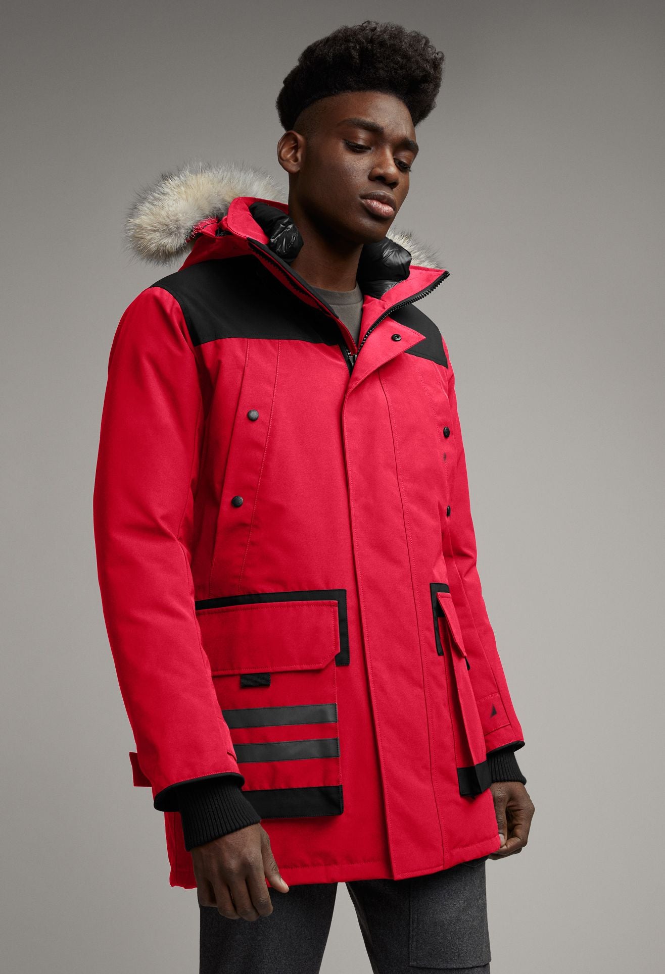 A male model wearing a red parka with a fur-trimmed hood and black accents.
