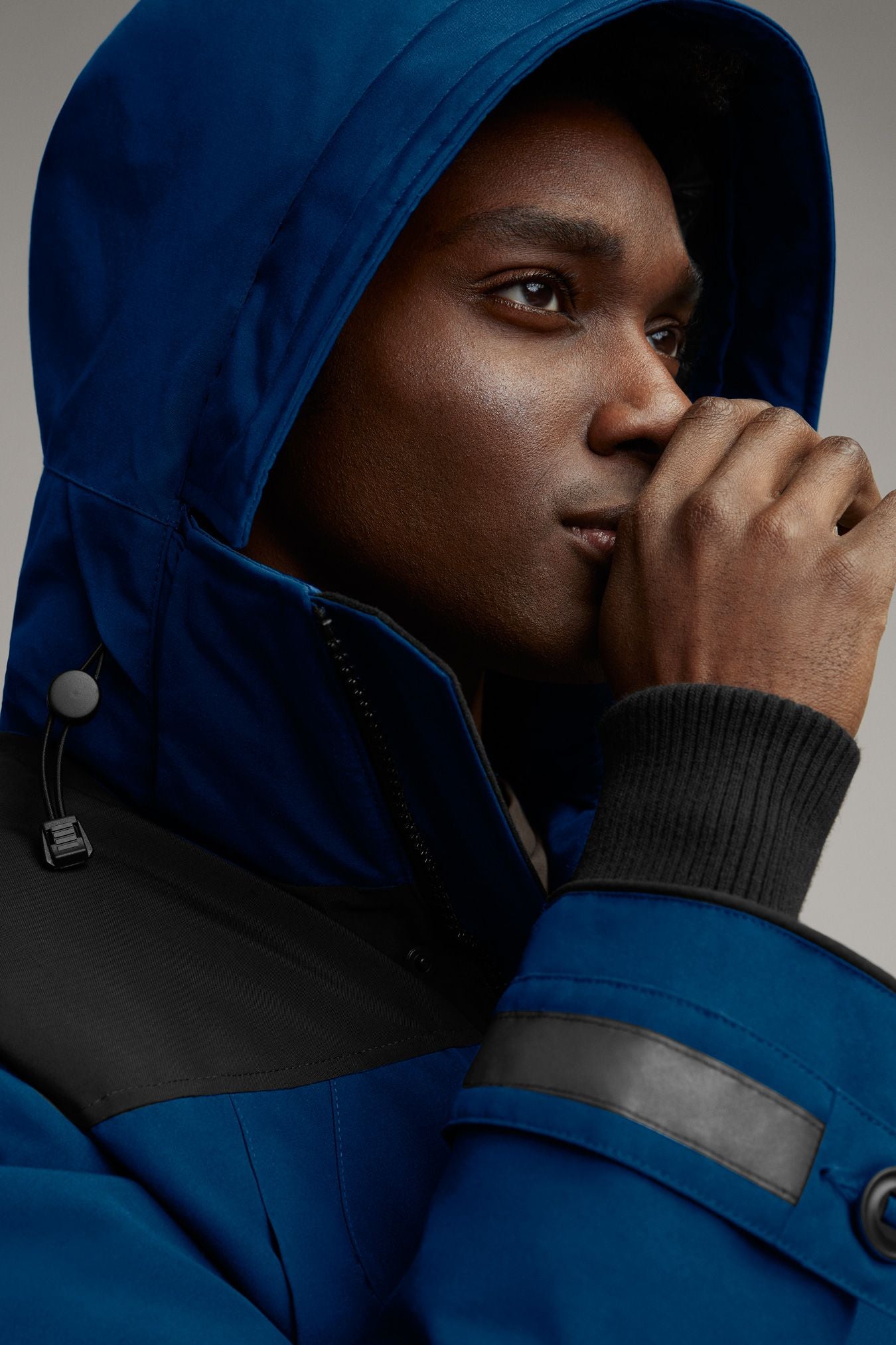 Person in blue hooded jacket, with black shoulder patches and dark wrist cuffs.