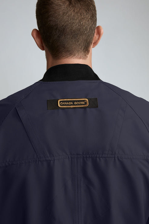 Back of a dark blue jacket with a black collar and a rectangular, gold-embroidered label.