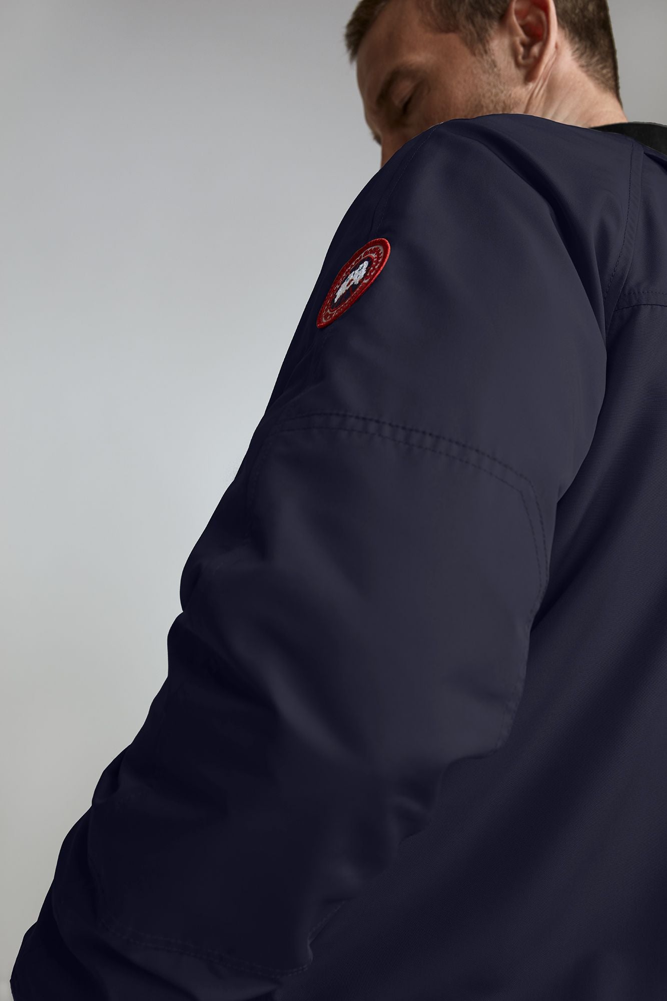 Close up of the arm of a dark blue jacket that has a circular, red and white patch on the upper arm.