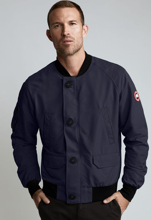 A man wearing a navy bomber jacket with black trim and button closure.