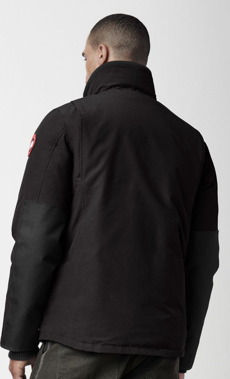 Back view of a black jacket with a high collar and logo on the sleeve.