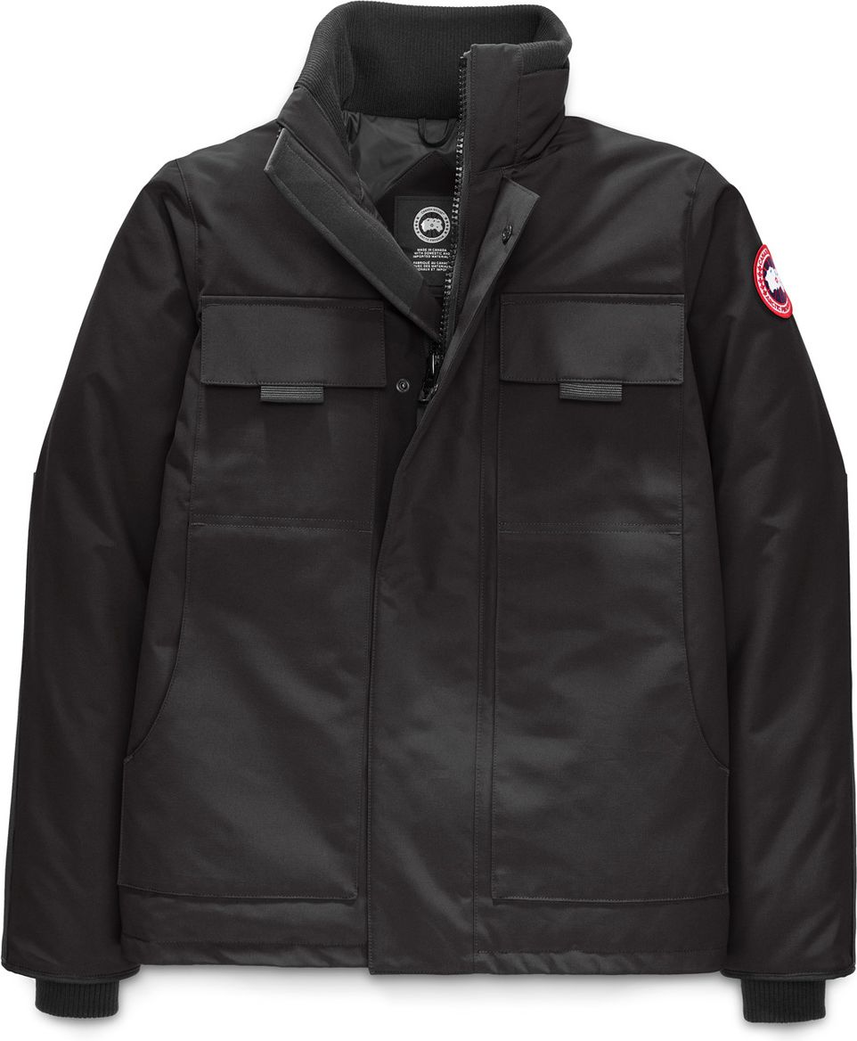 Black jacket with a stand-up collar, two flapped breast pockets, a circular logo patch on the upper left sleeve, and a snap-front closure.