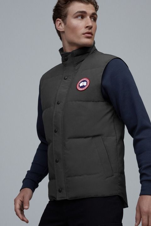 Man wearing a padded, dark green button-up vest with a red, white and blue circular logo on the chest.