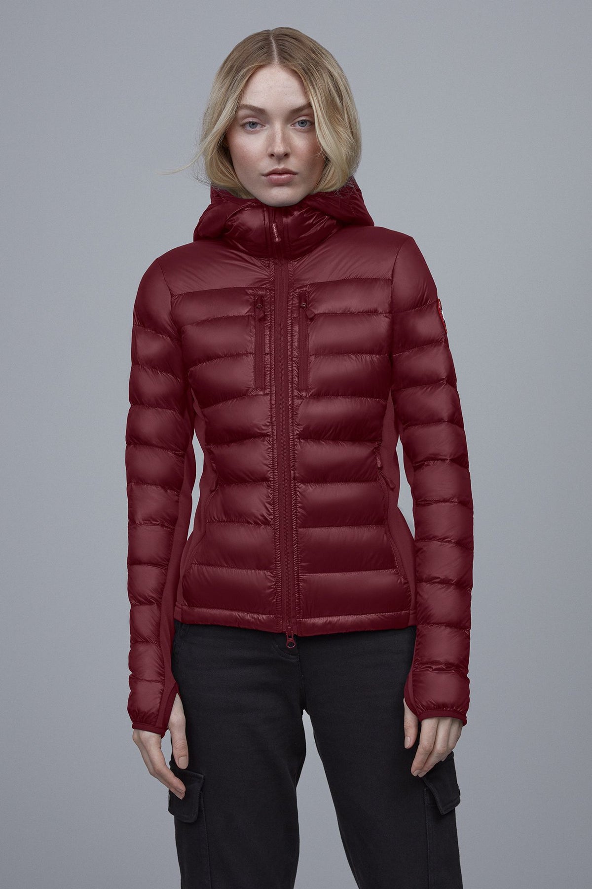 A person wearing a quilted red jacket with a hood and black pants.