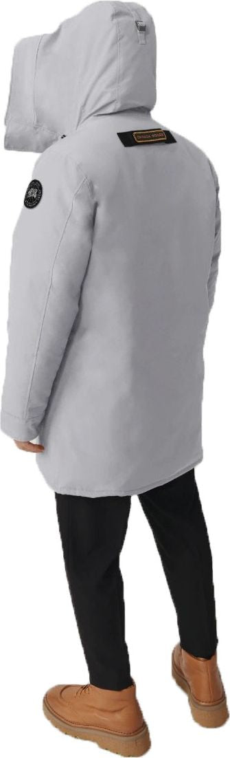 Back view of a person wearing a light gray parka jacket with a hood, black pants, and brown shoes.