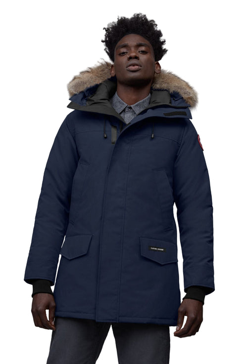 Man wearing a navy blue parka with fur-lined hood, front pockets, and emblem.
