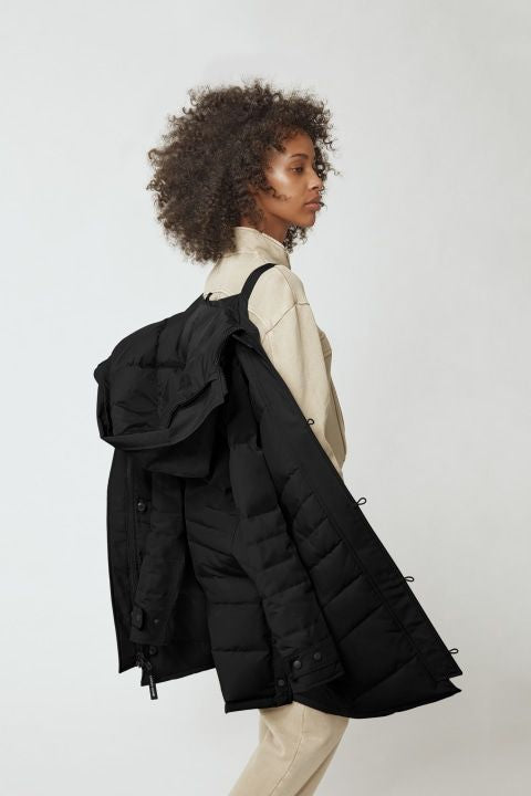 Woman wearing a beige top and pants with a black puffy coat hanging on her shoulder.