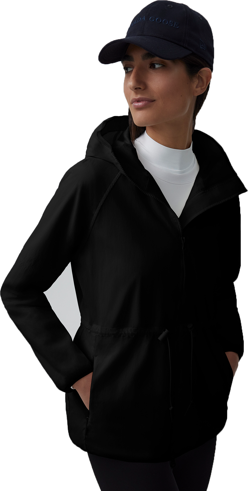 A woman wearing a dark baseball cap, a white long-sleeved shirt, and a black hooded jacket with a drawstring.