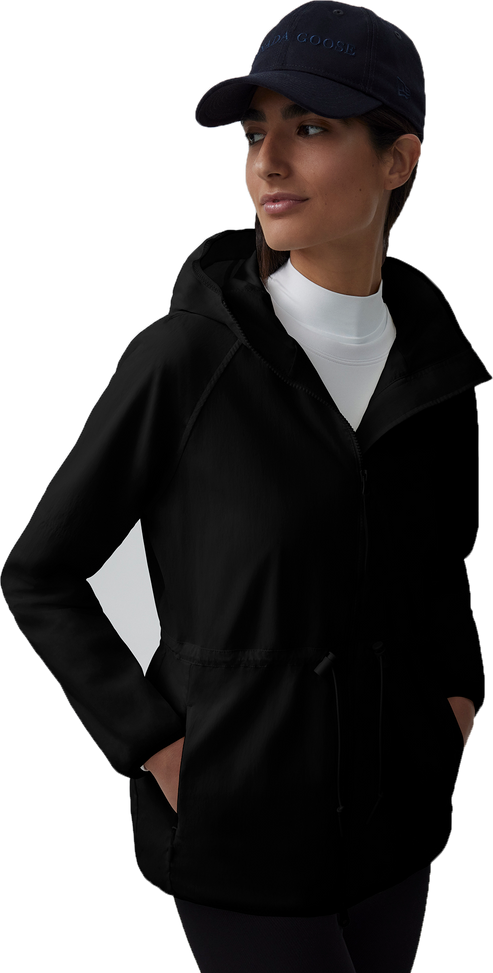 A woman wearing a dark baseball cap, a white long-sleeved shirt, and a black hooded jacket with a drawstring.
