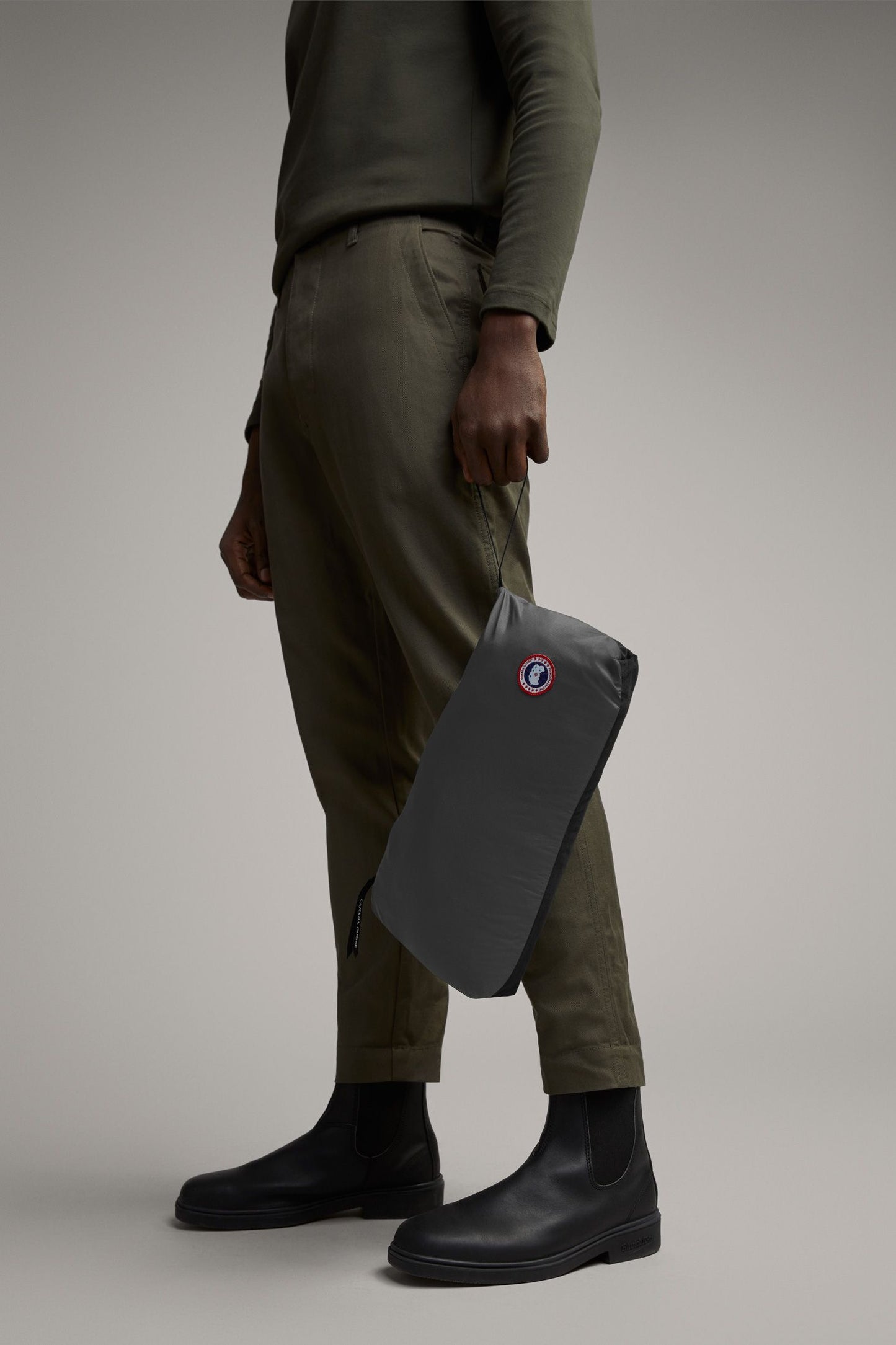 Person with gray pouch in hand, wearing black boots and green clothing.