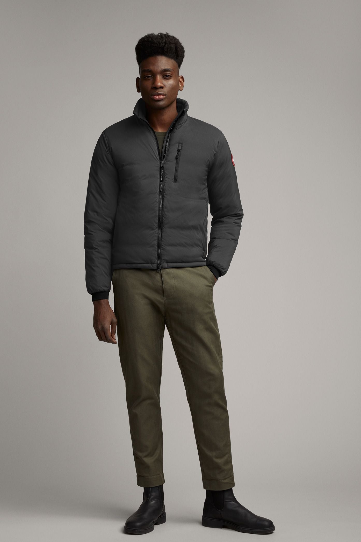 A man wearing a gray puffer jacket, green pants, and black shoes.