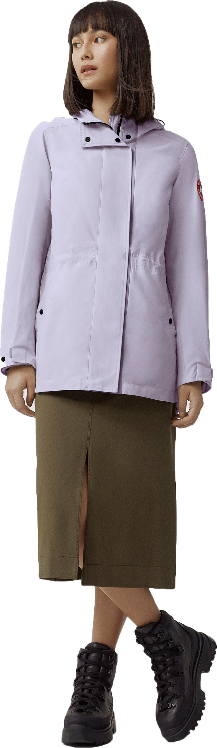 A woman wearing a lilac jacket, an olive-green skirt with a slit, and black combat boots.