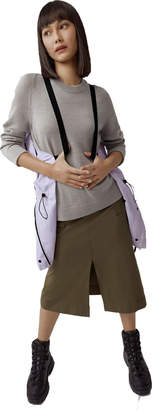 A woman with bangs wearing a gray sweater, olive skirt, black boots and suspenders over a light purple jacket.