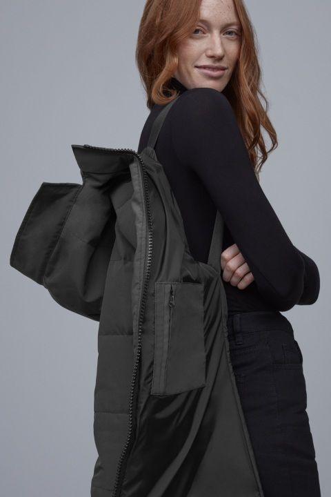 Woman in black turtleneck carrying open, puffy black coat over shoulder.