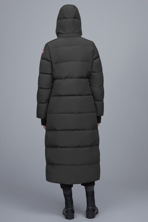 Rear view of a person wearing a full-length olive green down puffer coat with a hood, the left sleeve has a red and white patch.