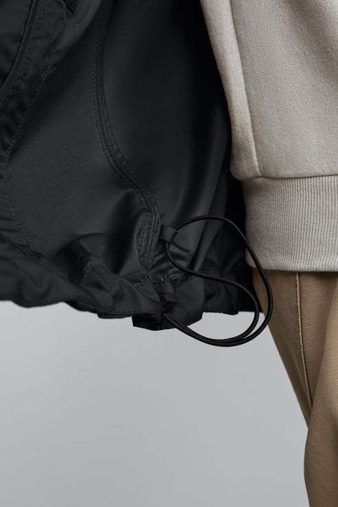 The hem of a black jacket has a drawstring next to a beige sleeve and pants.