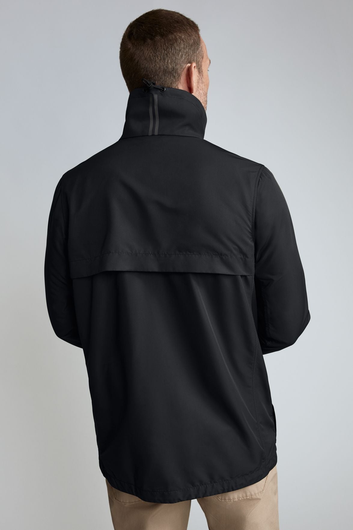 Rear view of a man wearing a black windbreaker jacket.