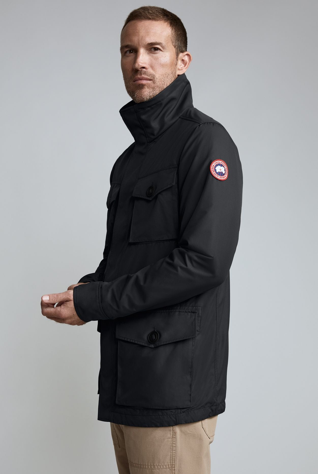 Man in black, hooded, four-pocket jacket with red, white, and blue circular patch on left arm.