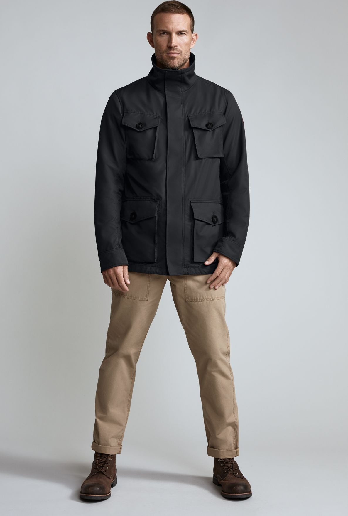 Man wearing a black field jacket with four front pockets and beige pants.