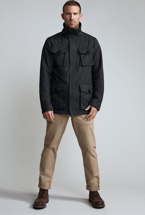Man wearing a black field jacket with four front pockets and beige pants.