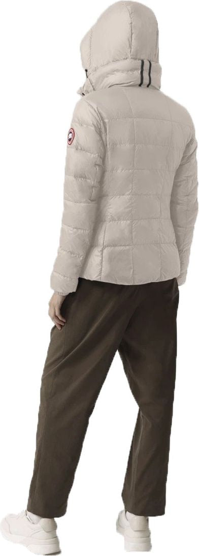 Person wearing a cream-colored puffer jacket with a hood and dark green pants.