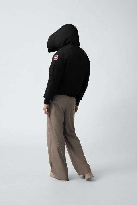 Person in black hooded jacket with logo on arm and brown pants.