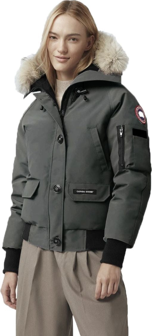 A woman wears a gray bomber jacket with a fur-lined hood, a black collar, and black cuffs.