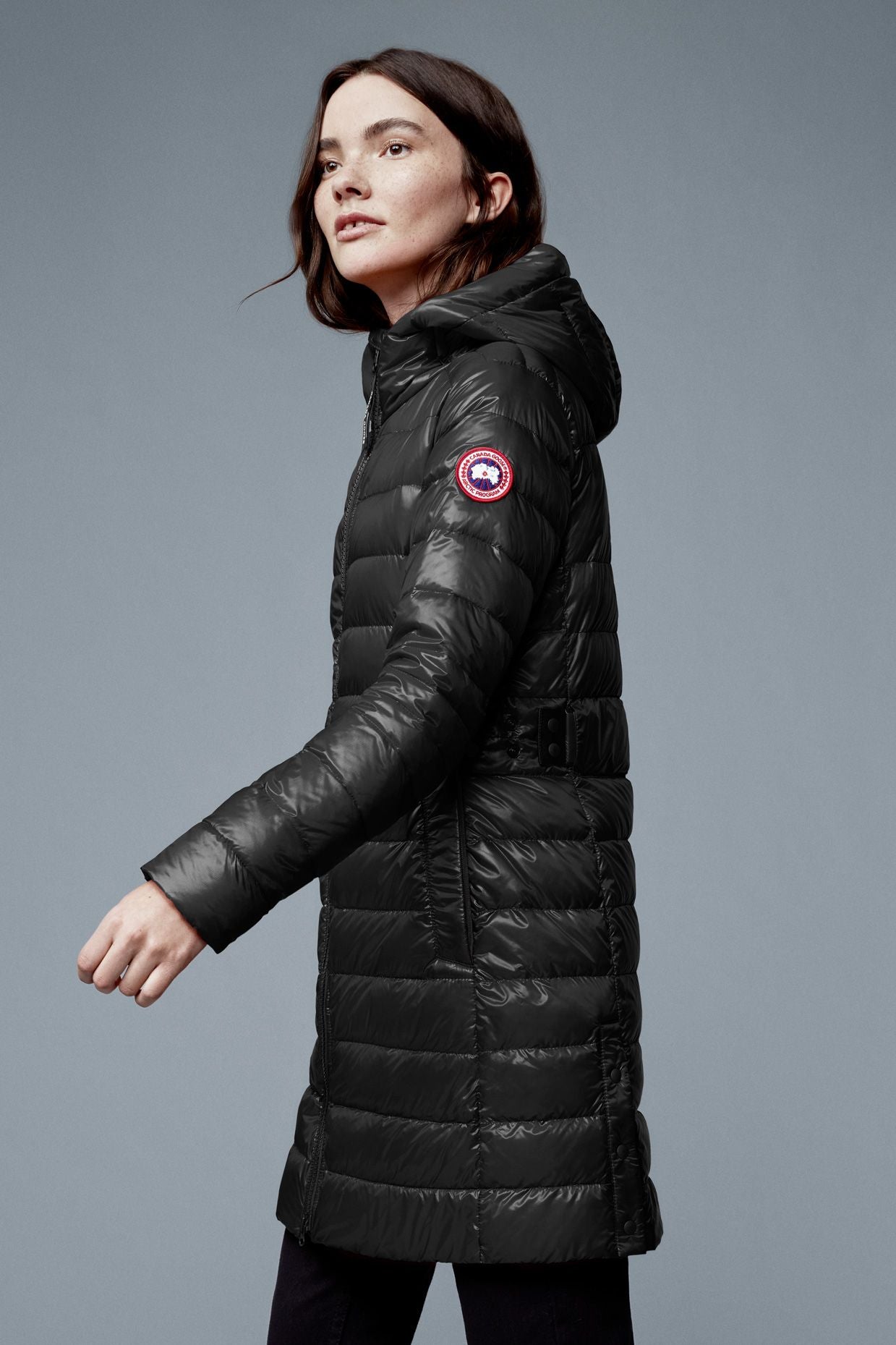 A woman wearing a long black puffy coat with a hood and a circular red, white and blue emblem on the arm.