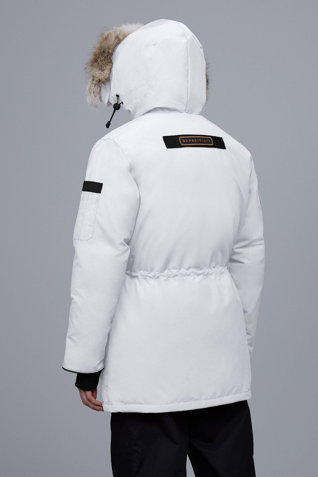 White parka with fur-lined hood and black logo patch on the back