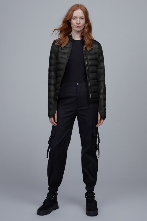 A woman with long red hair is wearing a black down jacket, black pants, and black shoes.