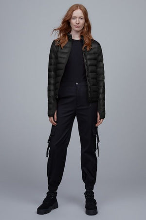 A woman with long red hair is wearing a black down jacket, black pants, and black shoes.