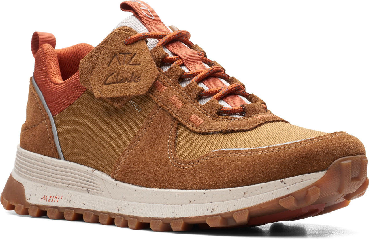 A tan sneaker with orange laces and a brown sole. The sneaker has suede and fabric panels and a white lining.