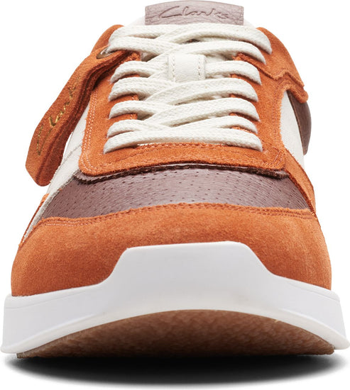 Close-up of a predominantly orange suede shoe with white laces and sole, featuring the word "clarks" on the tongue and side.