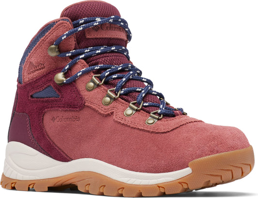 A hiking boot with a pink suede upper, maroon accents, blue and white laces, gold-tone metal hardware, a white midsole, and a brown outsole.