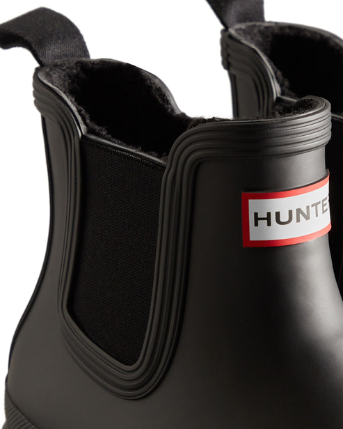 Close up of black ankle boot showing elastic gusset and the word HUNTER on a red and white patch.