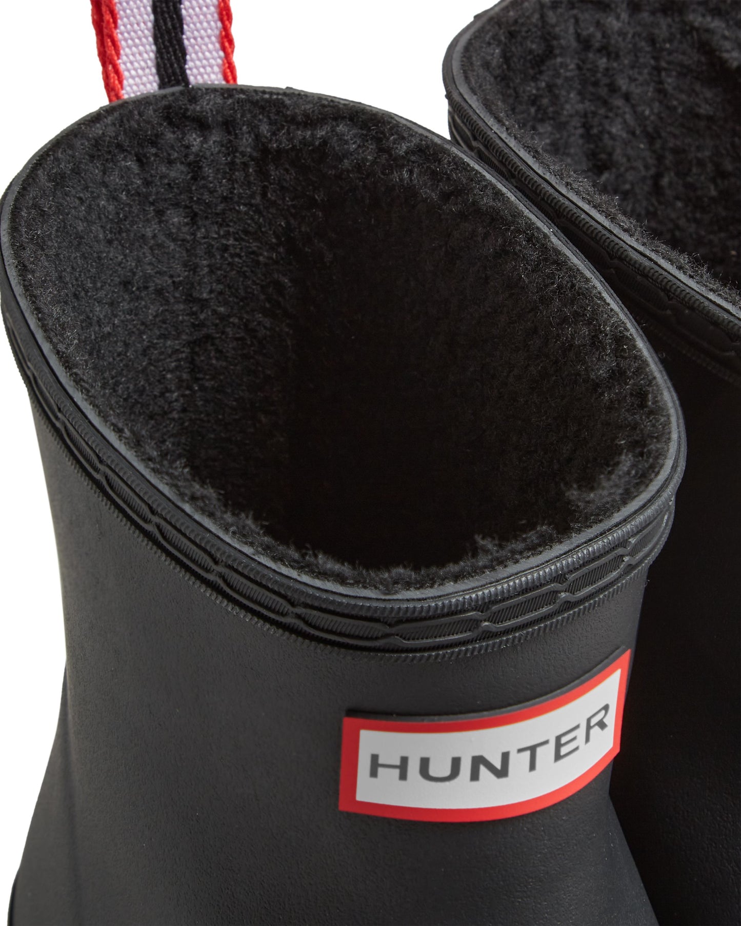 Close-up of the opening of a black rain boot with black shearling liner and red and white tag.