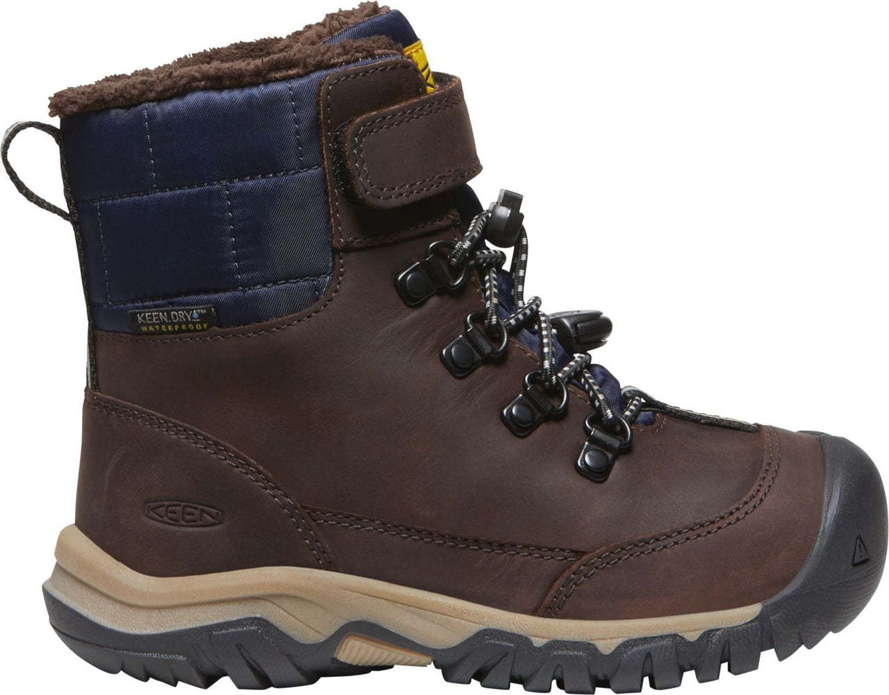 A brown leather snow boot with a velcro strap, metal eyelets, black and white laces, a navy blue quilted nylon cuff, and a faux fur lining.
