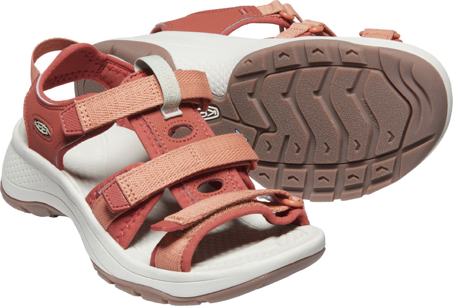 A pair of terracotta and peach adjustable velcro strap sandals with white soles.
