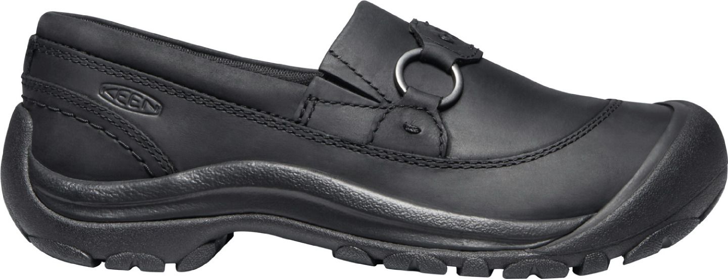 A black slip-on shoe with a rubber sole and a round metal ring on the upper.