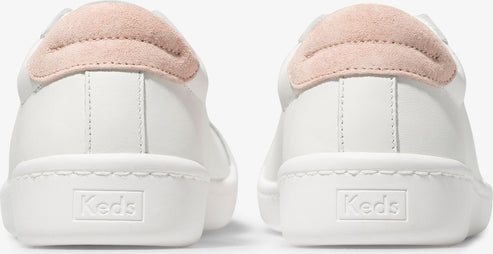 Back view of white sneakers with 'Keds' embossed on the heel and pink suede heel tabs.