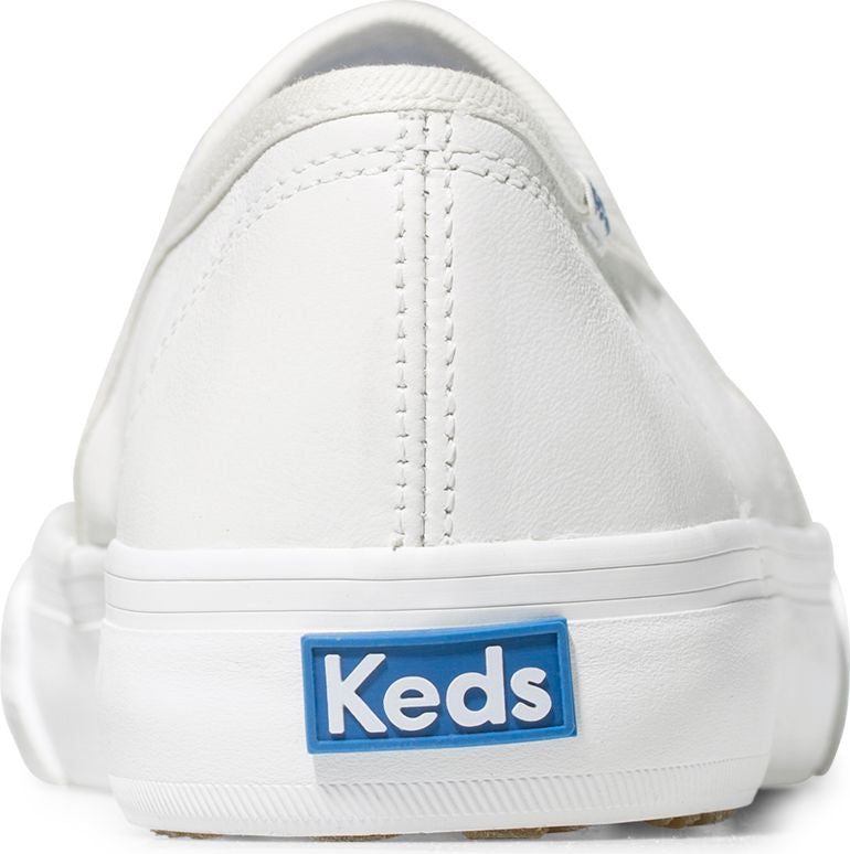 Close-up of the back of a white sneaker with a blue and white logo that says "Keds".