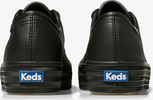 The backs of a pair of black leather sneakers with a platform sole and a blue logo that reads, Keds.
